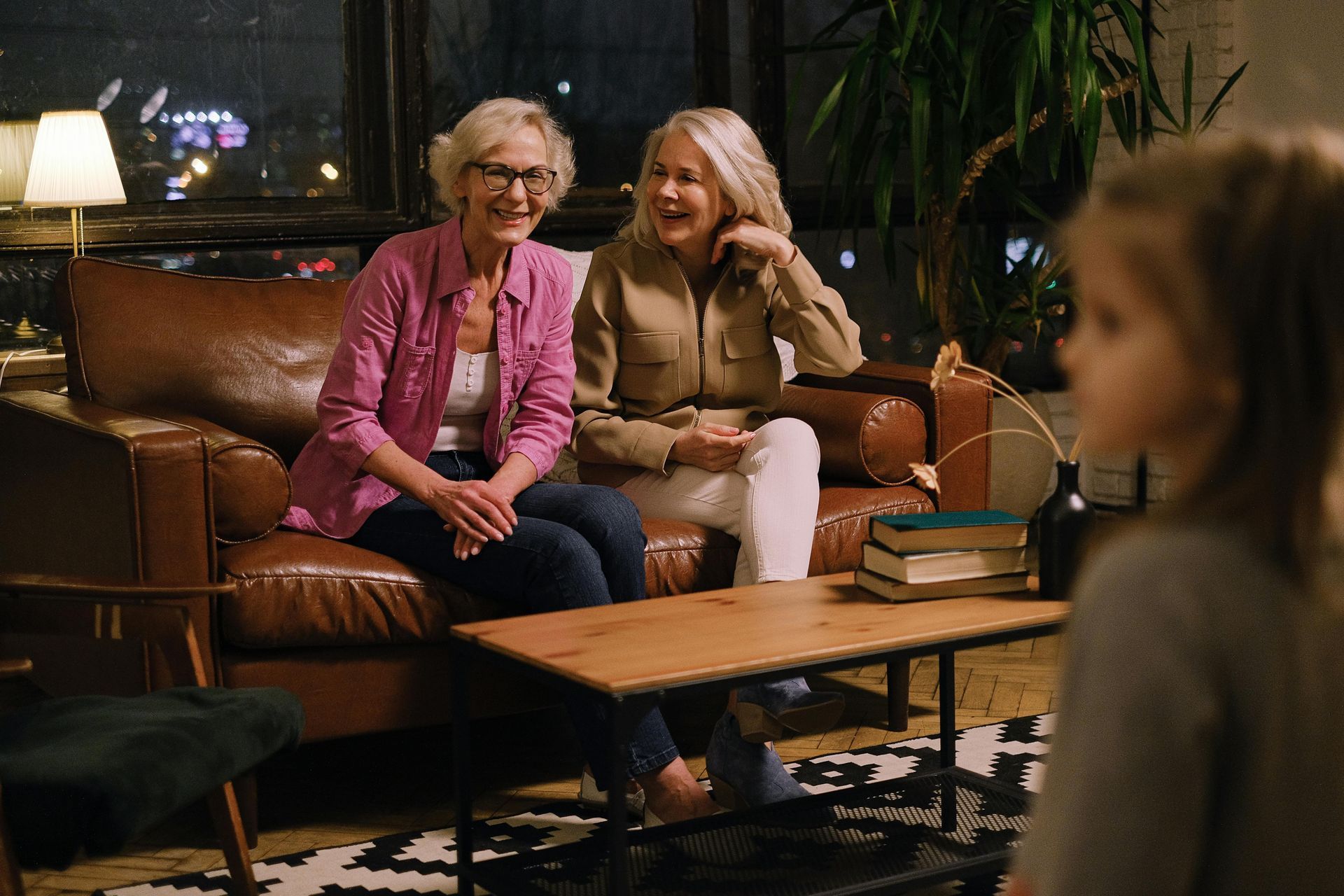 Family in a grassy park: parents smiling, holding a baby in yellow overalls. Trees in background.
