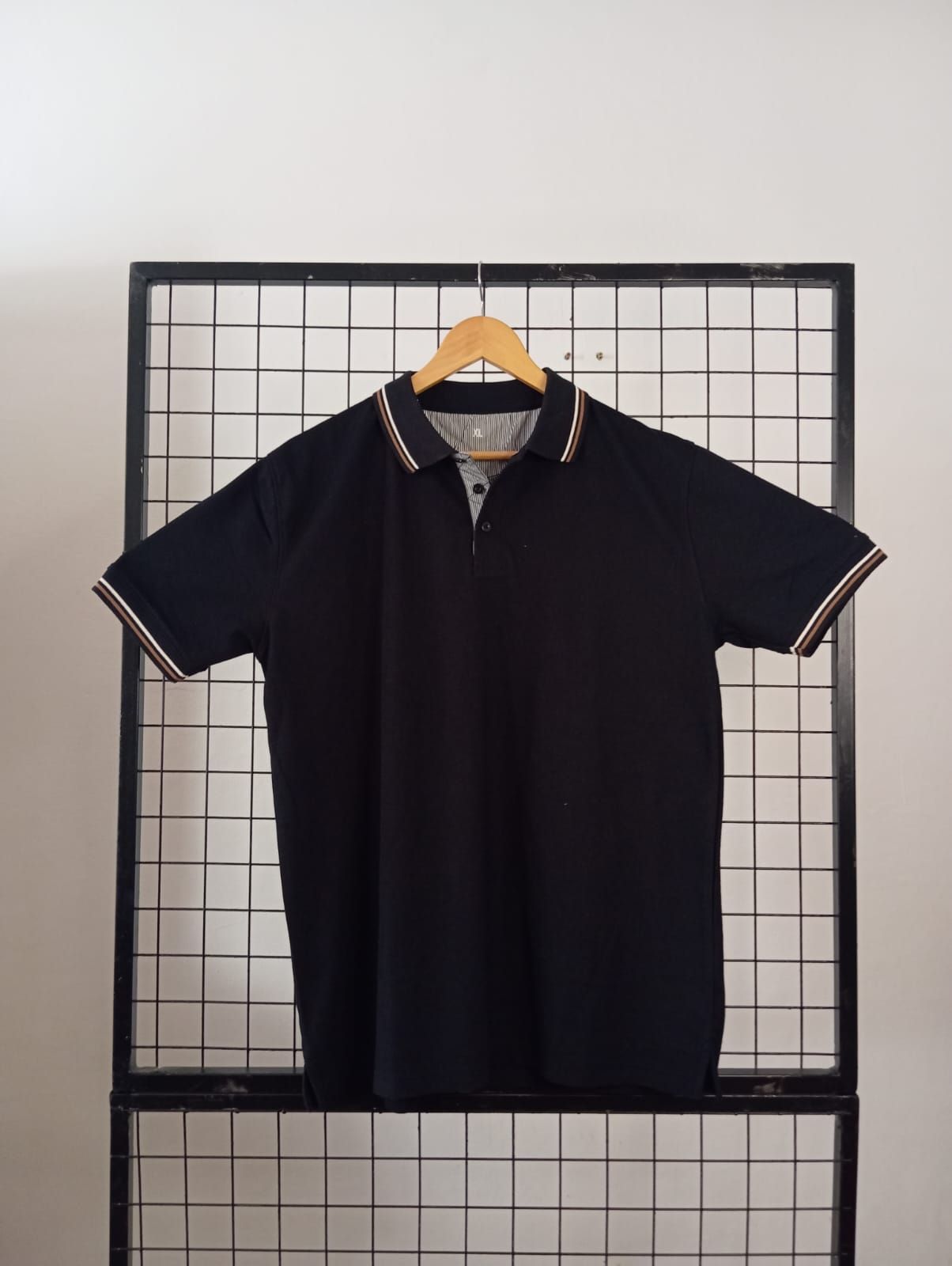 Polo blanco colgado sobre una rejilla negra contra una pared blanca.