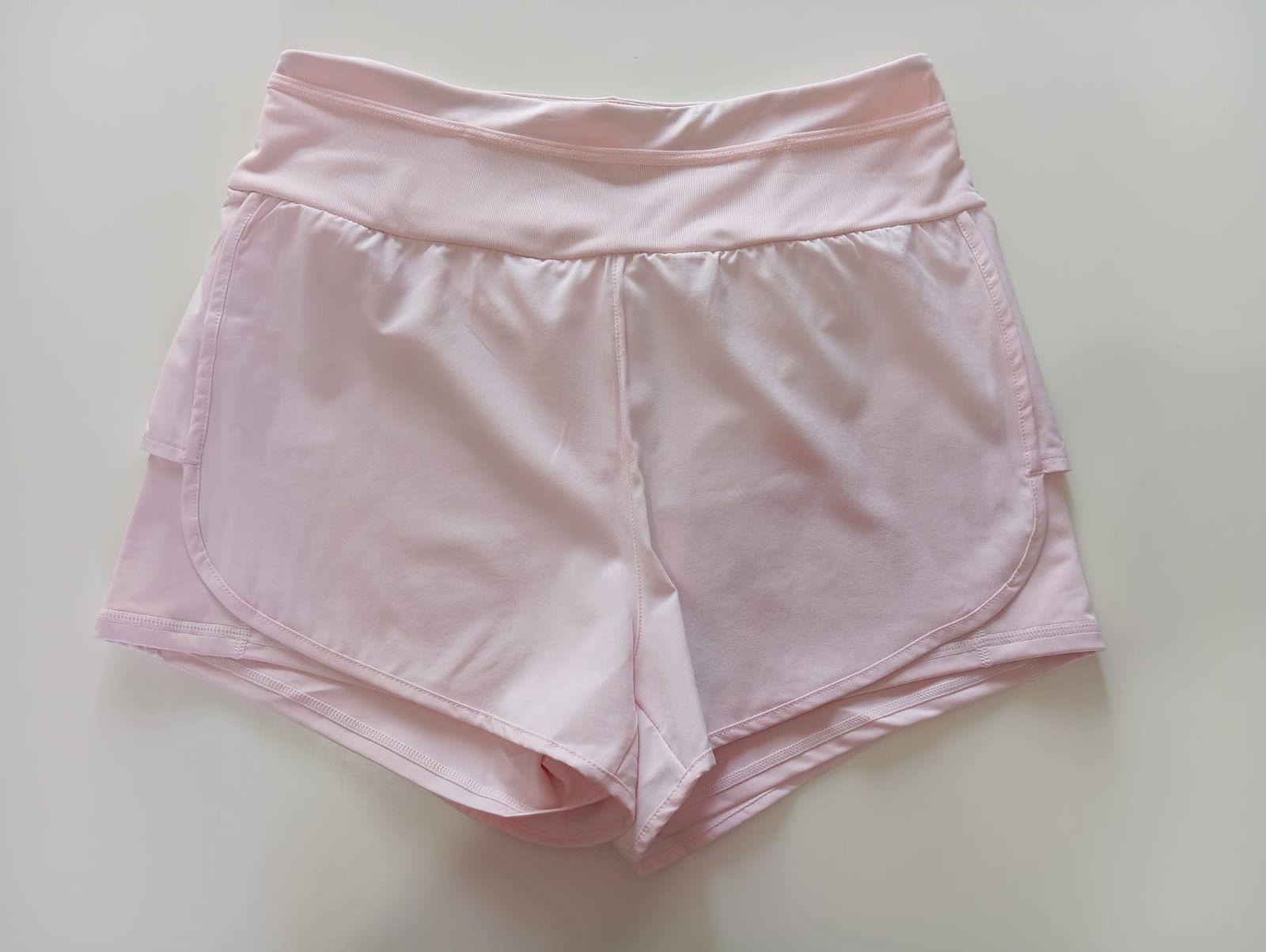 Pila de pantalones cortos deportivos en varios colores: azul claro, rosa, azul marino, beige, negro y azul claro.