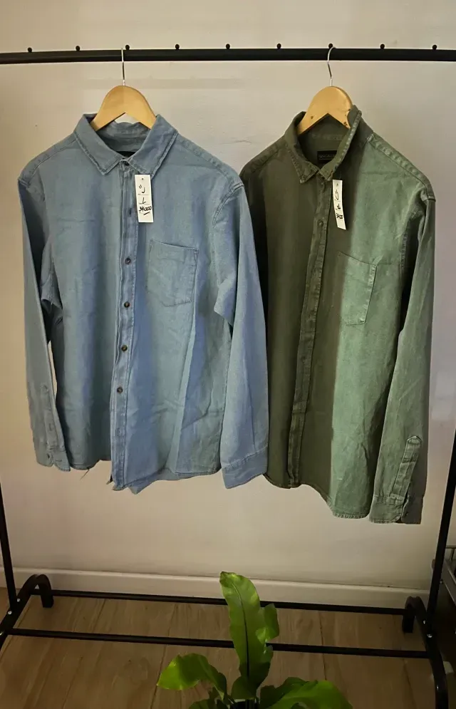 Dos camisas abotonadas, una azul y otra verde, colgadas en un perchero.