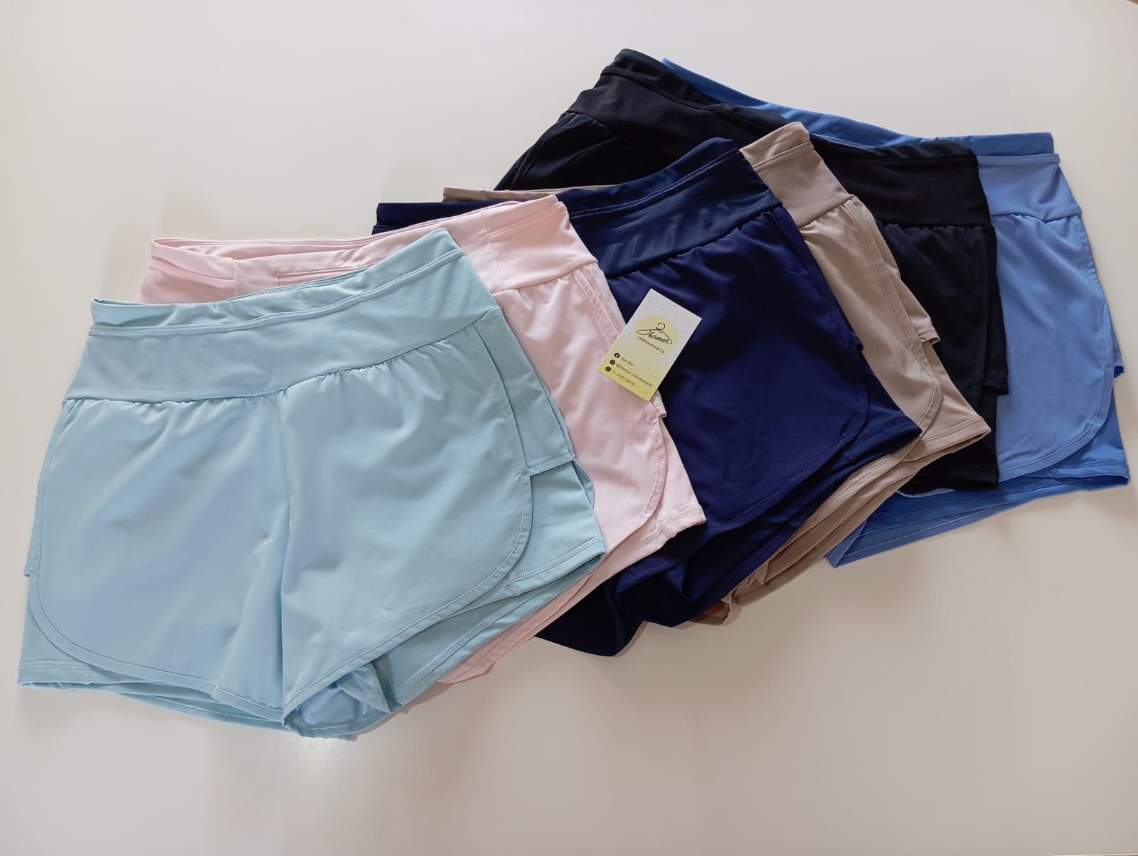 Pila de pantalones cortos deportivos en varios colores: azul claro, rosa, azul marino, beige, negro y azul claro.