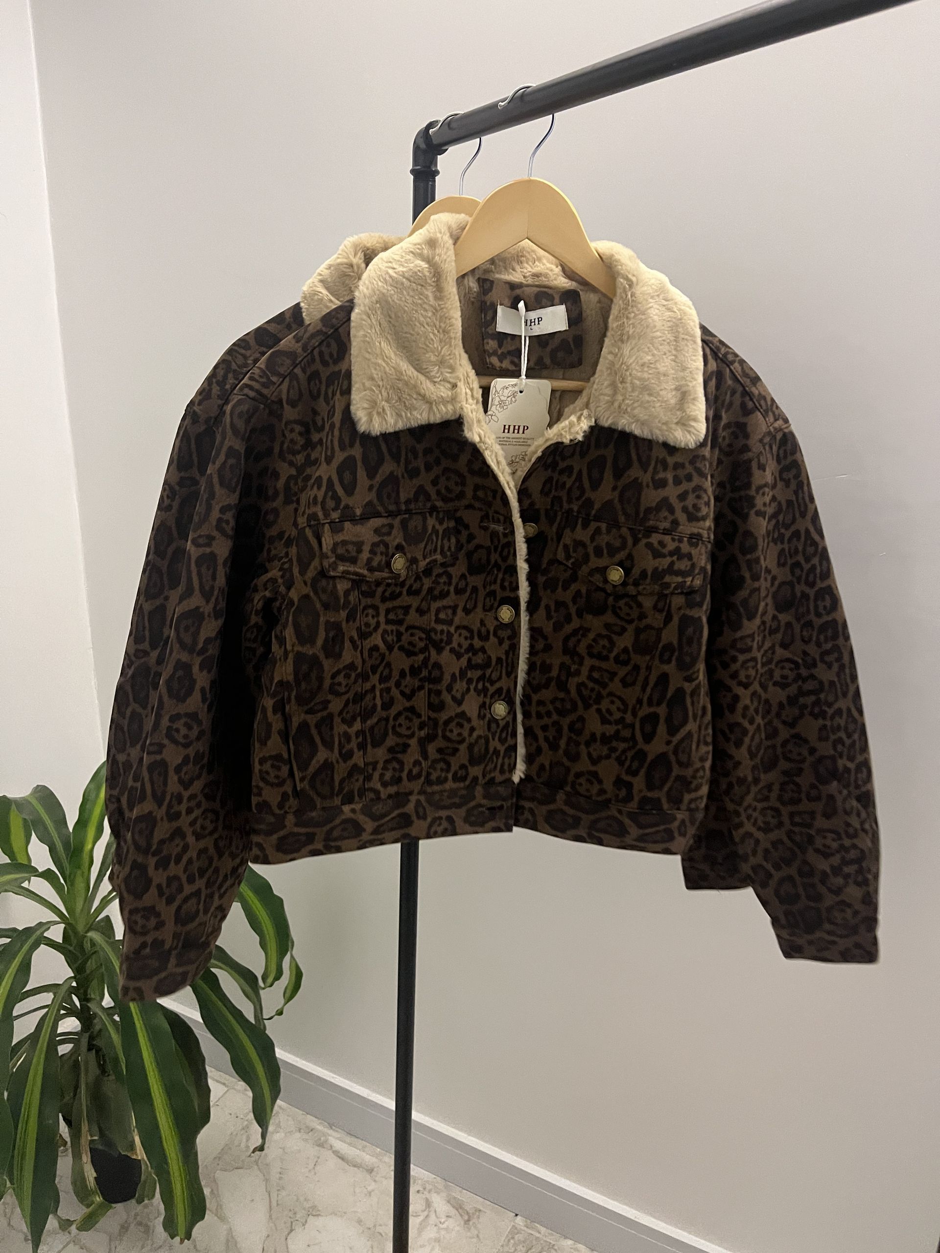 Chaqueta marrón con estampado de leopardo y cuello de sherpa color canela, colgada en un perchero metálico.