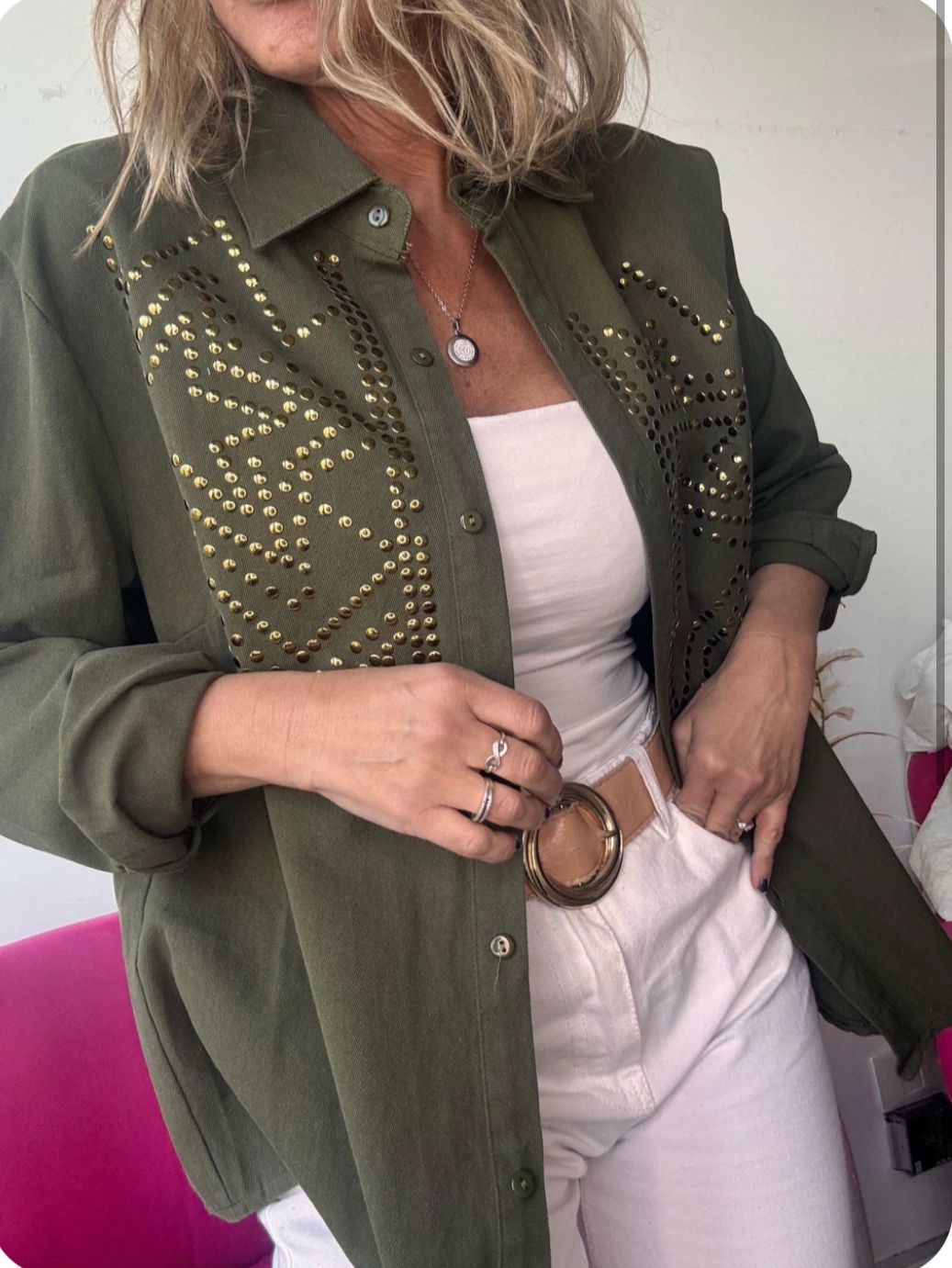 Mujer que lleva una chaqueta negra con tachuelas sobre una blusa y pantalones blancos, con un cinturón negro.