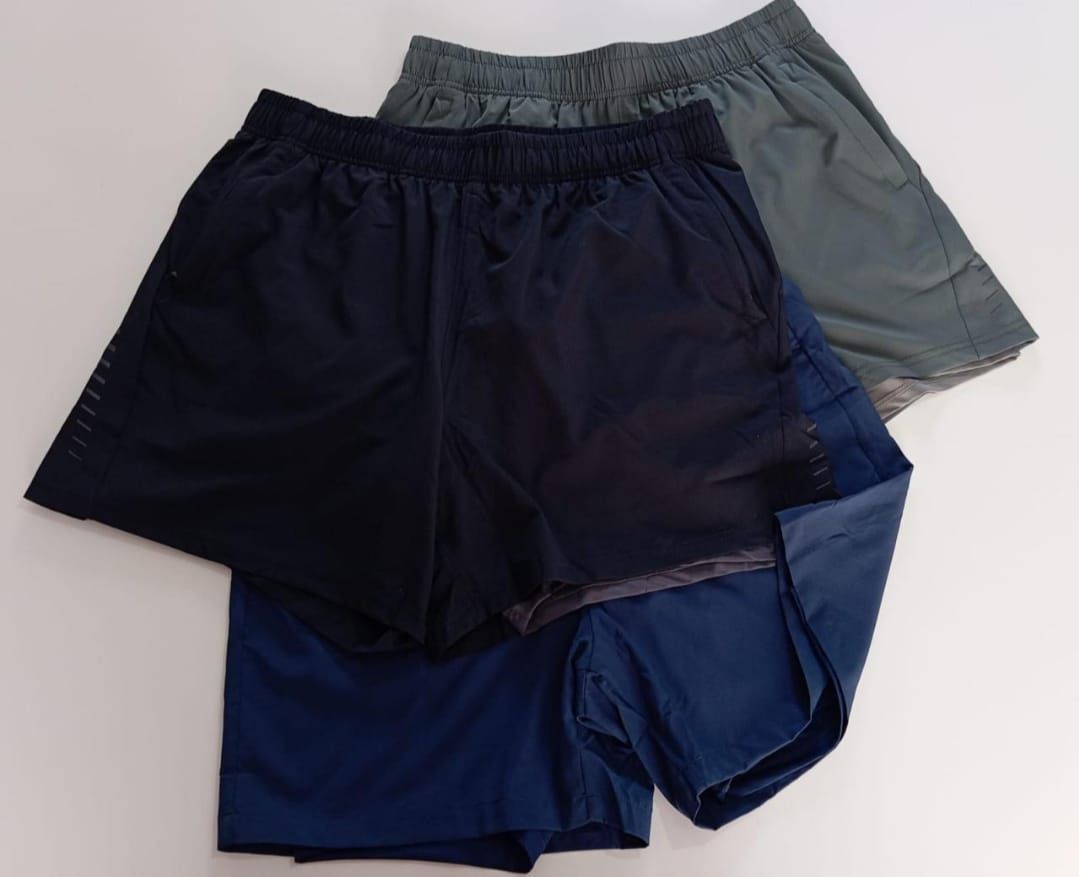 Tres pantalones cortos deportivos, azul marino, azul oscuro y gris, dispuestos sobre una superficie blanca.