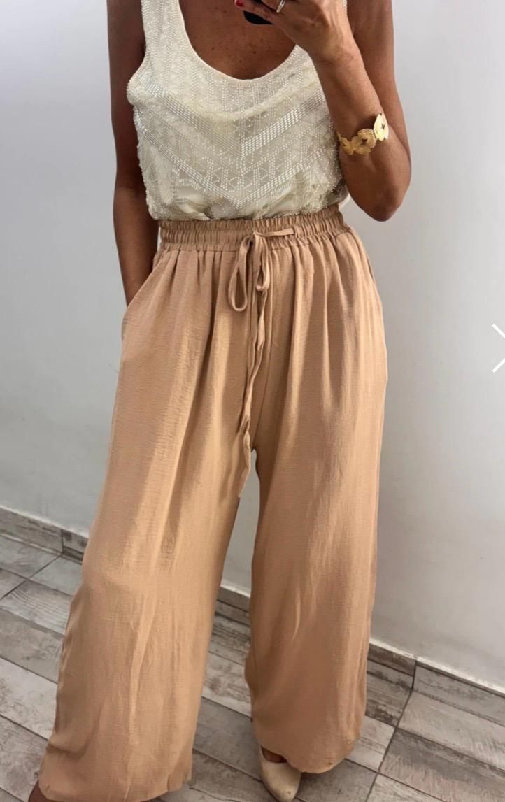 Mujer con mono negro con bordado color crema en el corpiño, manos en los bolsillos.