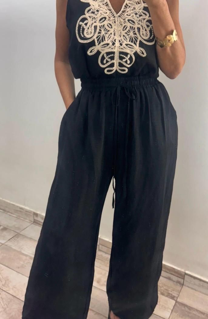 Mujer con mono negro con bordado color crema en el corpiño, manos en los bolsillos.