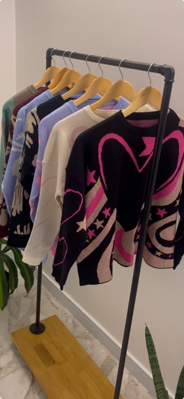 Perchero con varios jerseys: negro con corazón rosa, celeste, blanco y otros.