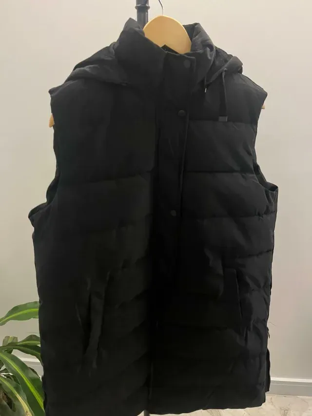 Chaleco acolchado con capucha negra colgado en una percha de madera.