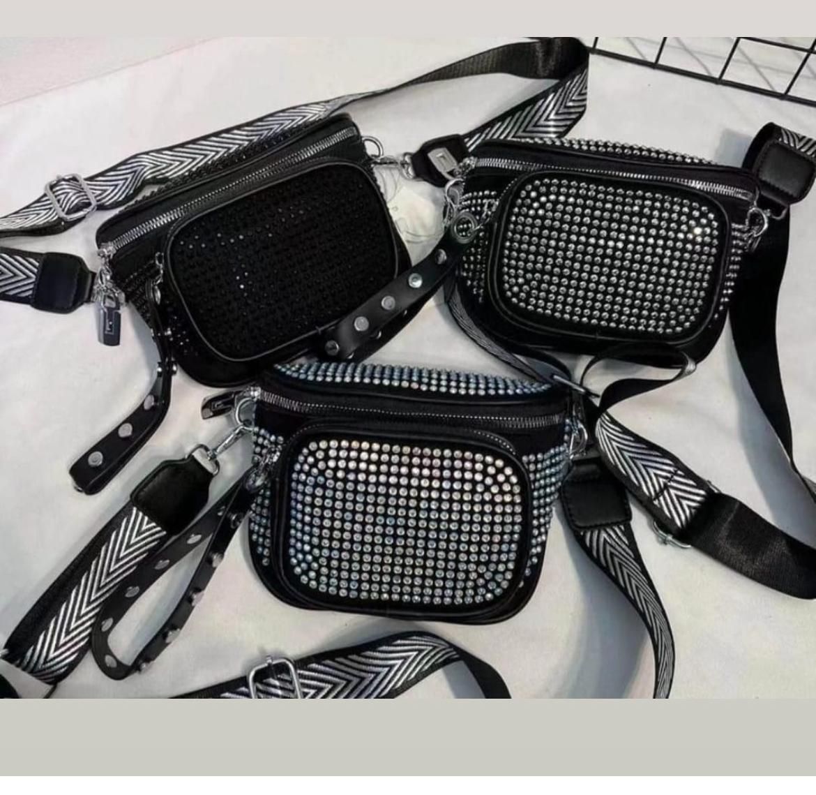 Tres bolsos bandolera negros con detalles de pedrería y correas estampadas.