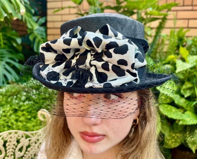 Woman wearing a black hat with a large white spotted bow and veil.