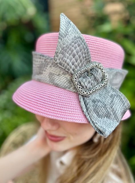 Pink straw cloche hat with snakeskin band and buckle. Woman's head and shoulders are visible, blurred background.