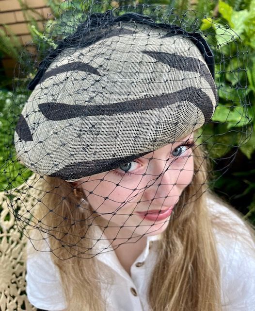 Woman wearing a hat with black zebra stripes, covered with a black veil.