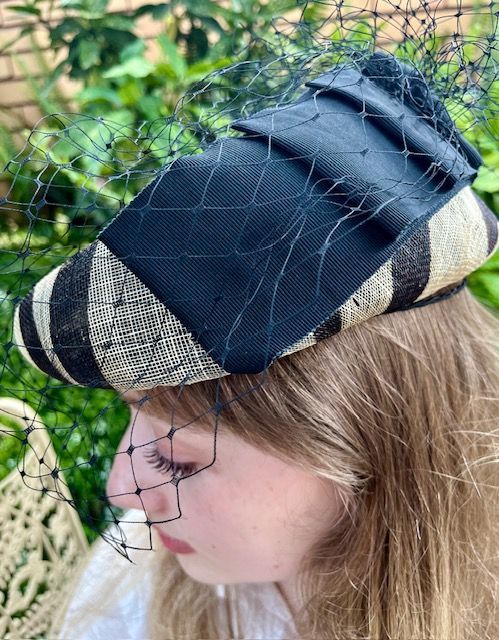Woman wearing a black and beige striped hat with a black netting veil.