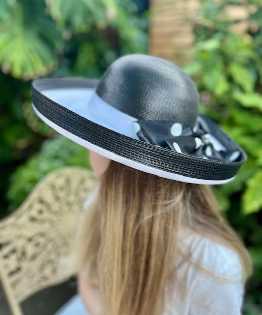 Woman wearing a black and white sun hat with a polka dot bow.