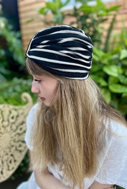 Woman wearing a black and white striped turban, outdoors near green foliage.