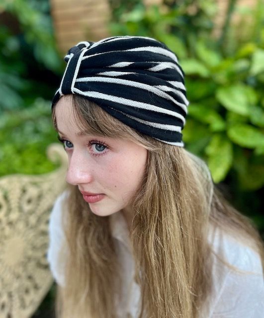 Girl wearing a black and white striped turban, outdoors, looking away.