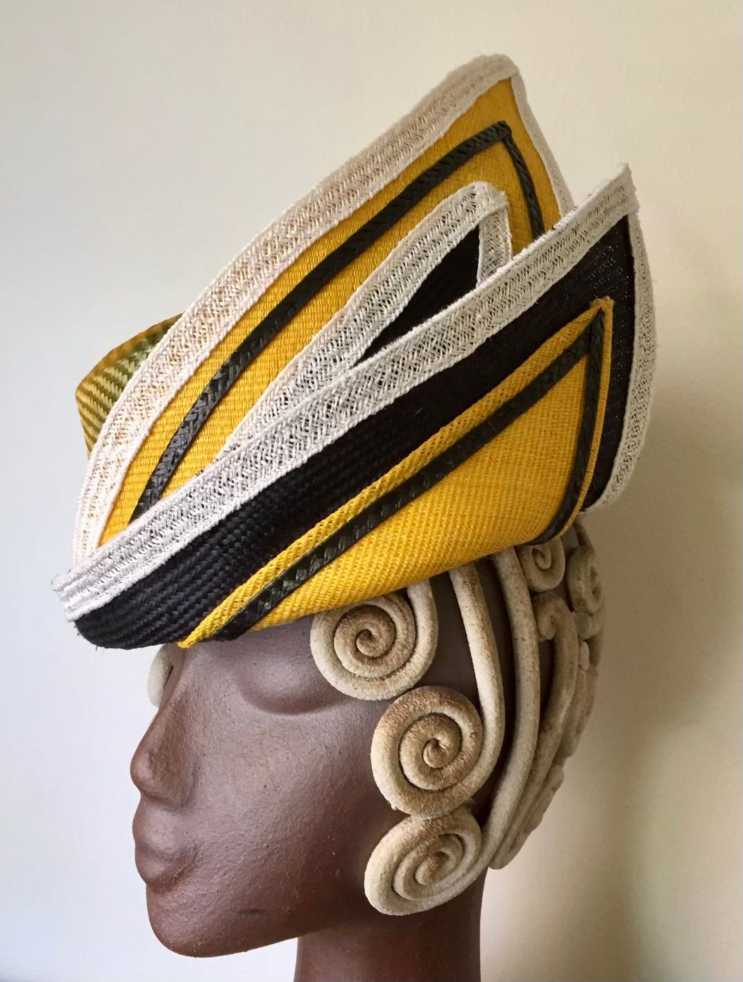 A sculptural headpiece featuring yellow, black, and white angled patterns, over a mannequin head with decorative swirls.