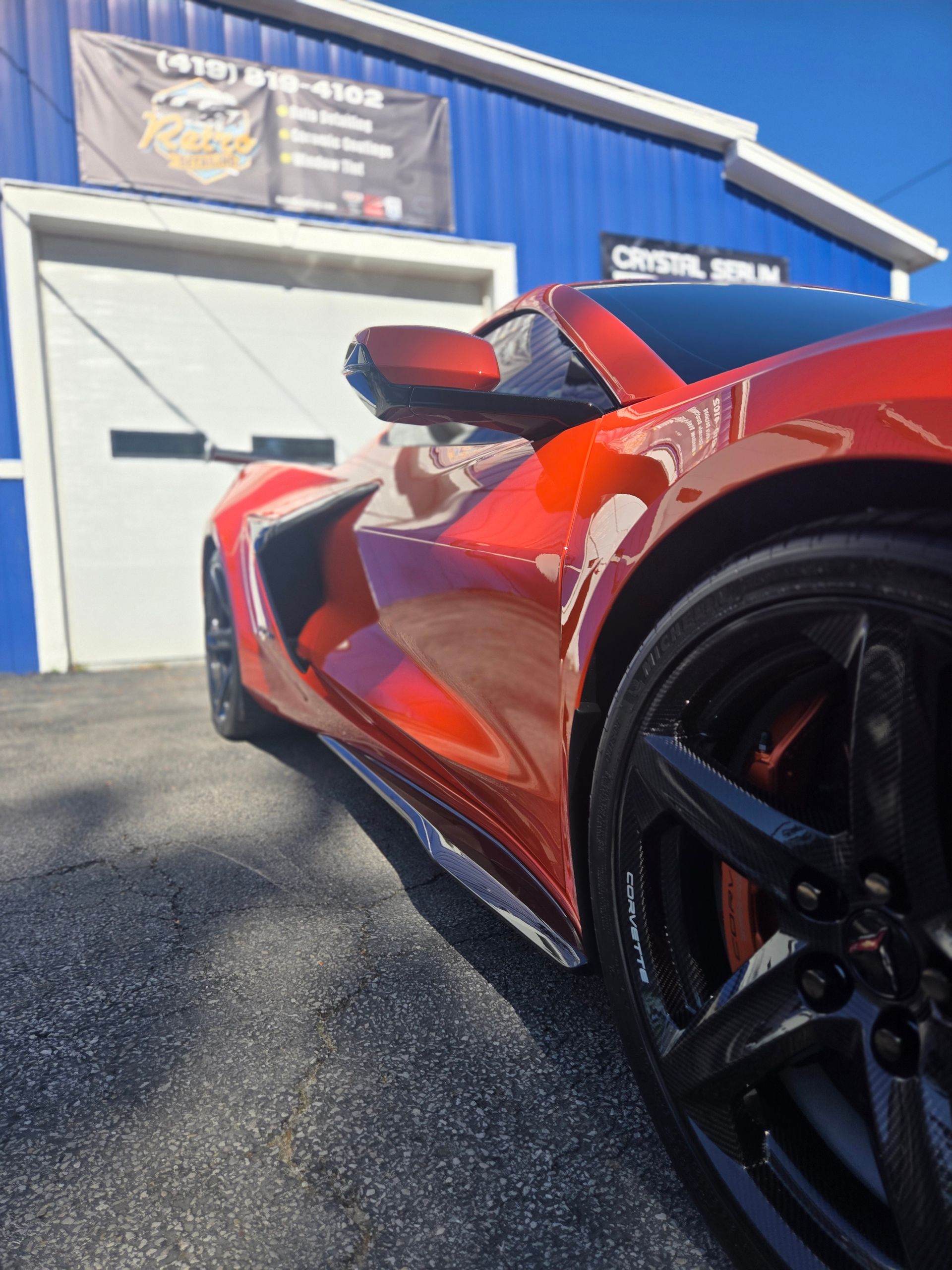 Red sports car parked outside a blue auto shop on a sunny day
