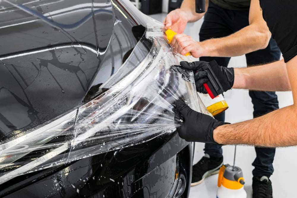 Workers applying clear protective wrap to a black car door