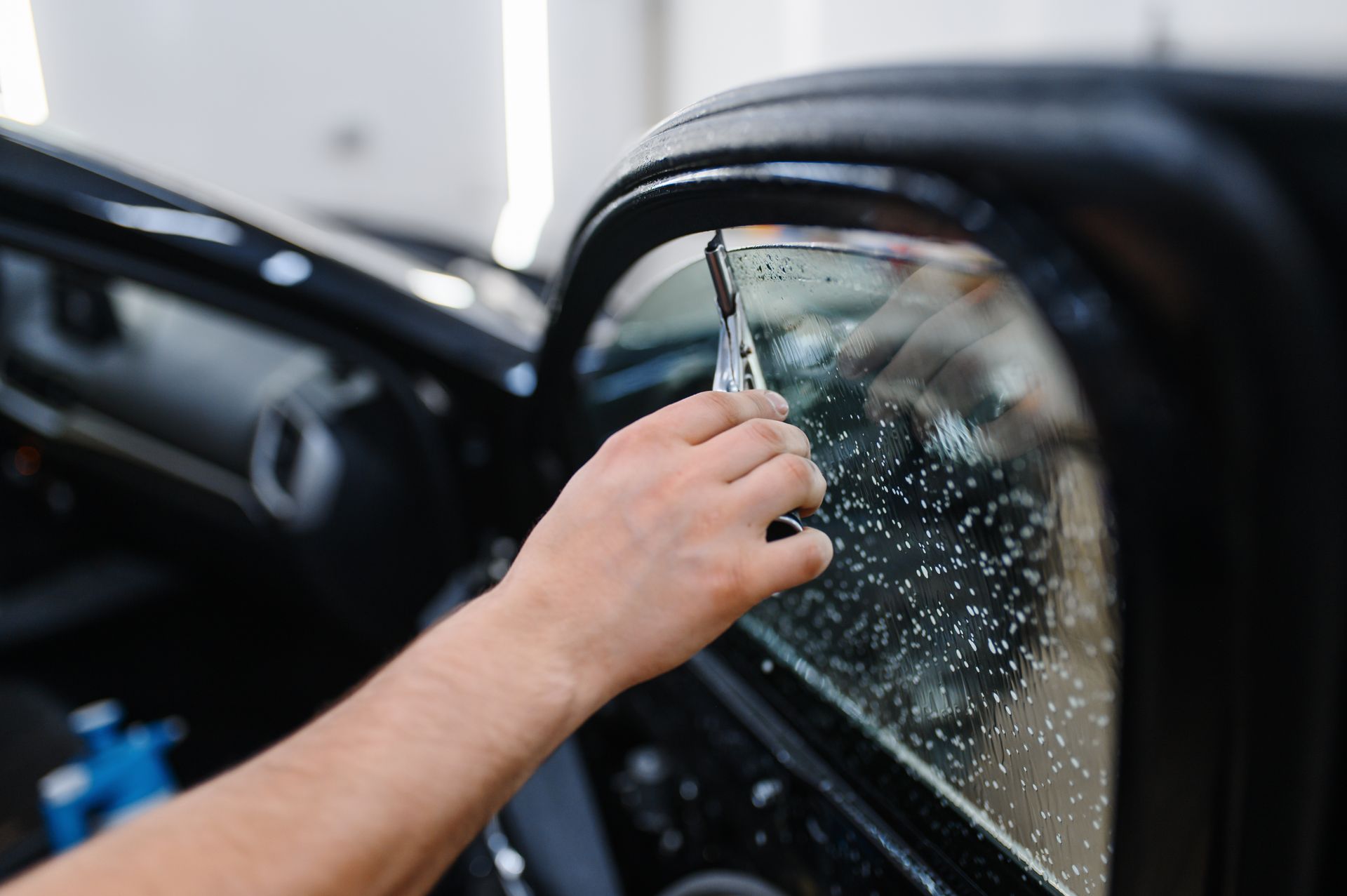 Hand cleaning a car side mirror with a squeegee, water droplets visible on the glass