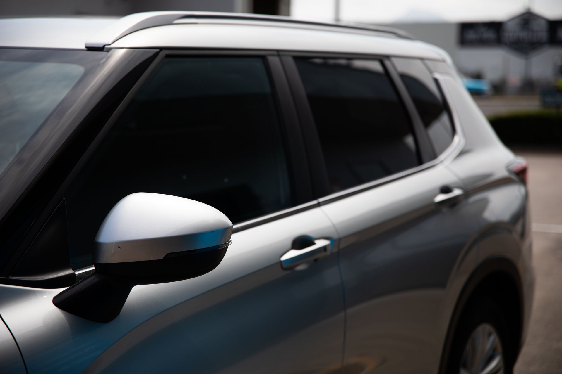 Silver SUV side view with tinted windows and white side mirror parked outdoors