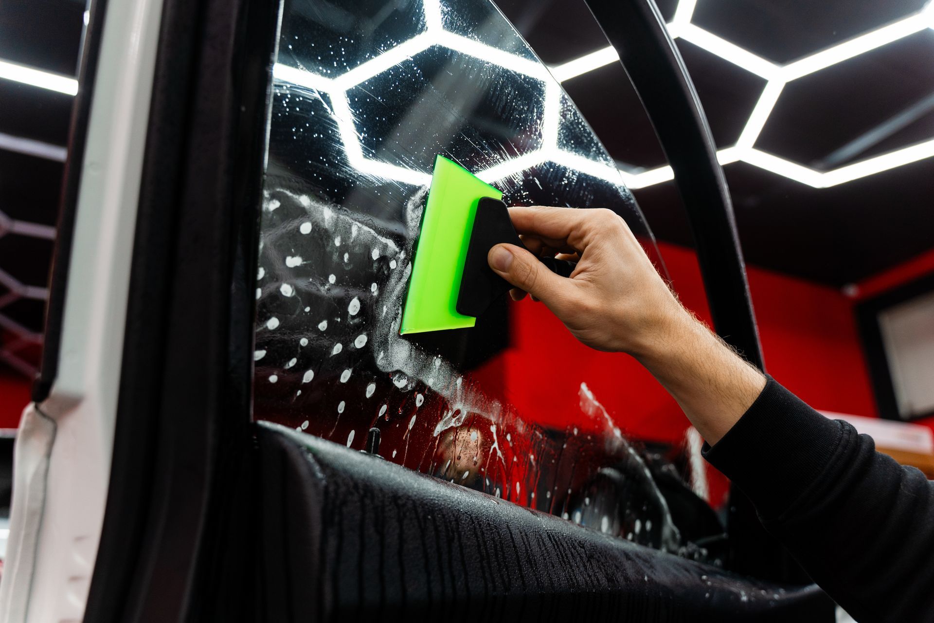 Hand cleaning a car window with a green sponge, with water and reflections on the glass