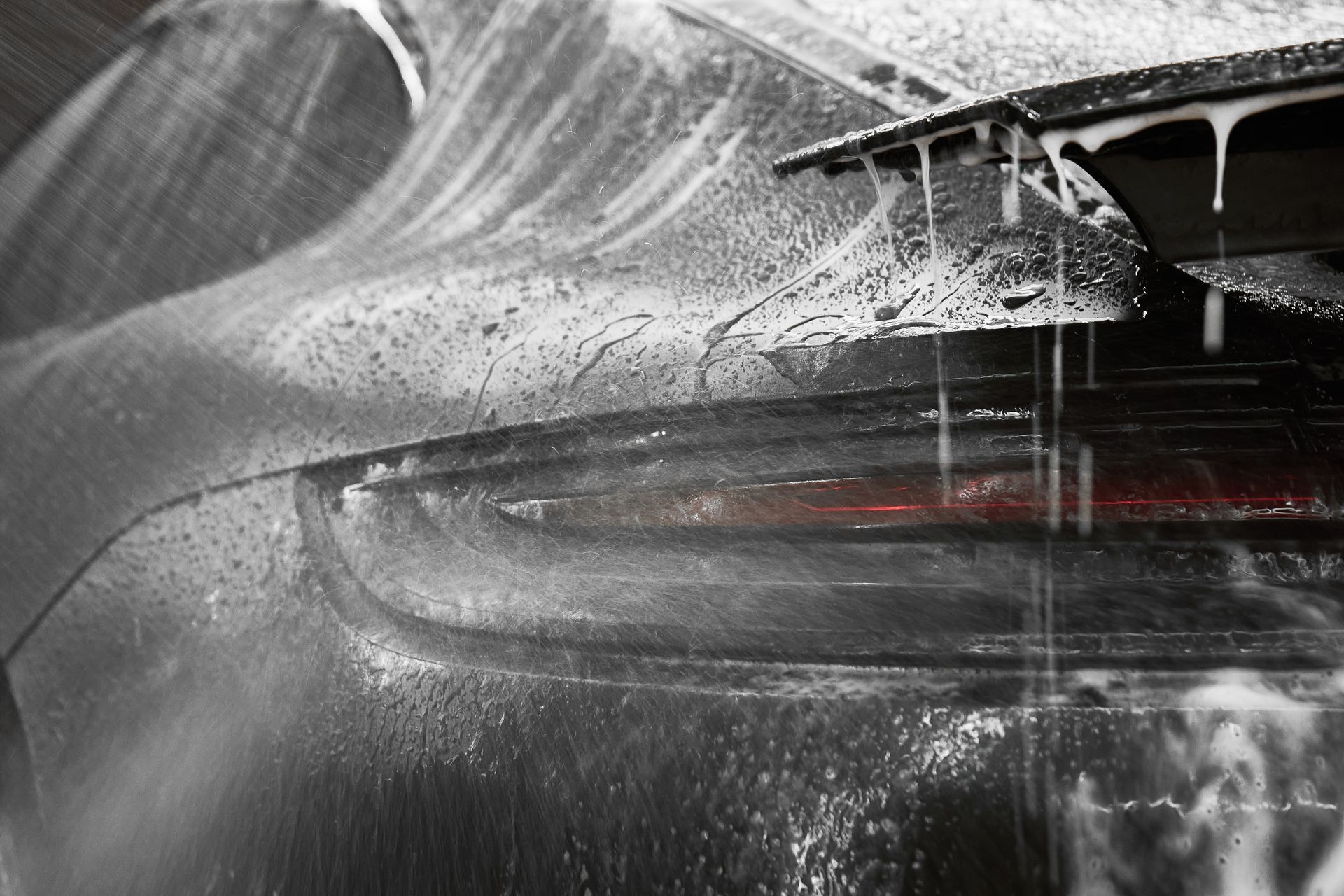 Sports car being washed in heavy water spray, rear taillight glowing red.