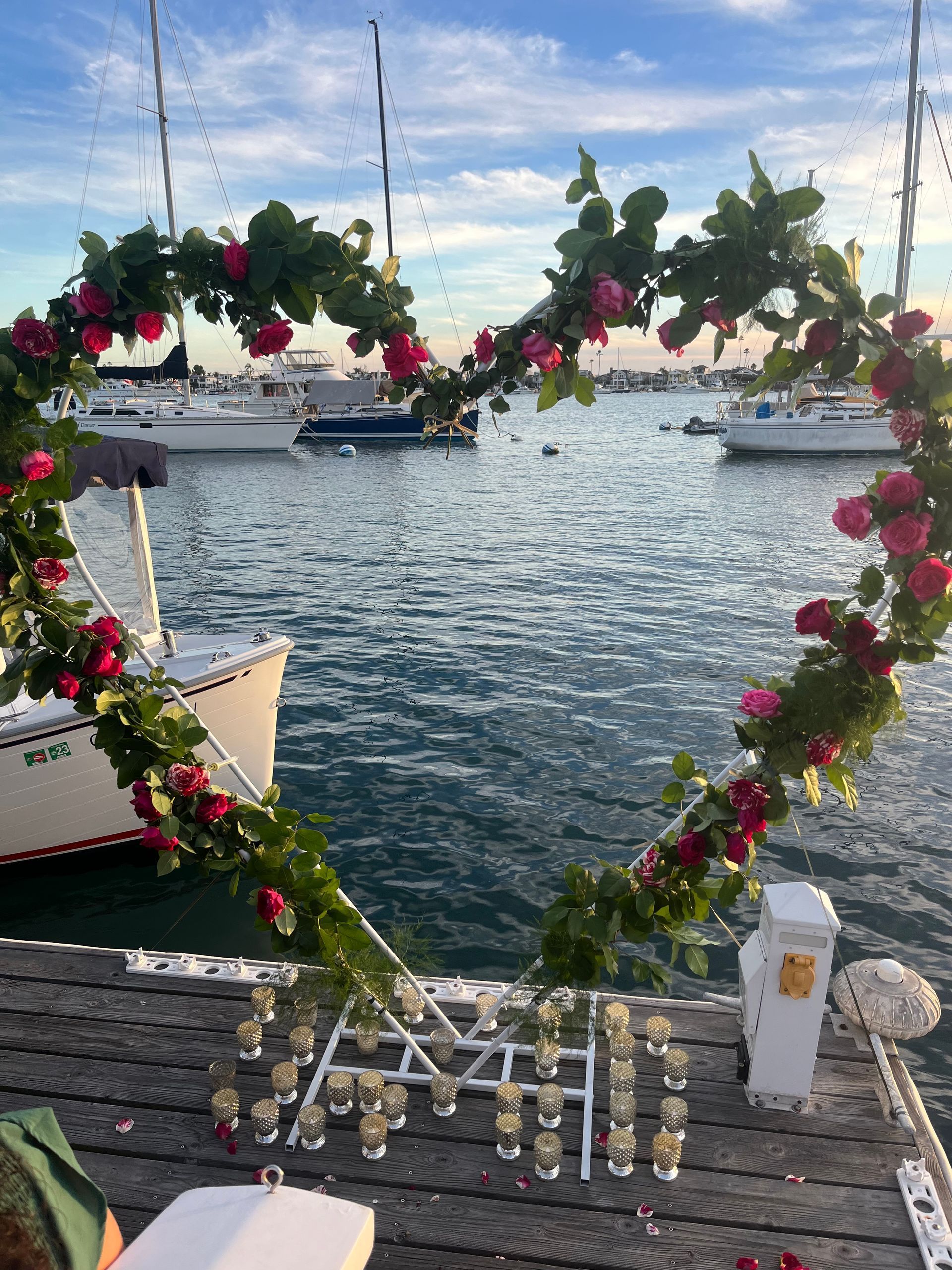A dock decorated with flowers and candles with boats in the background.