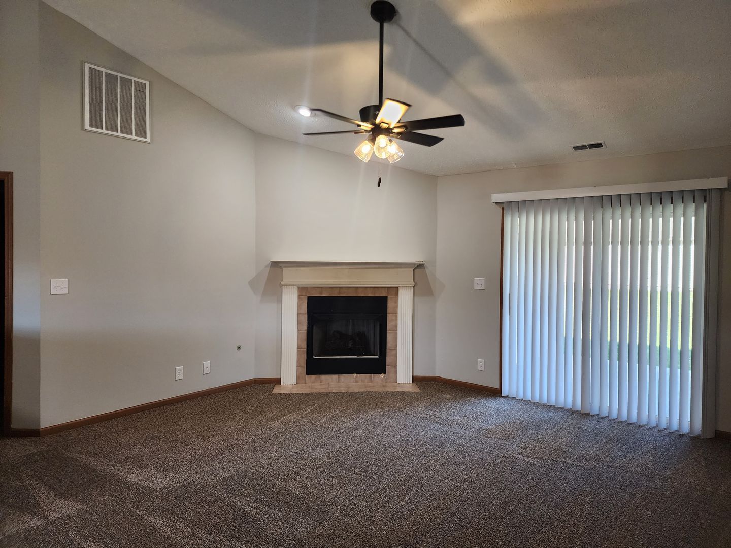 an empty living room with a fireplace and a ceiling fan .