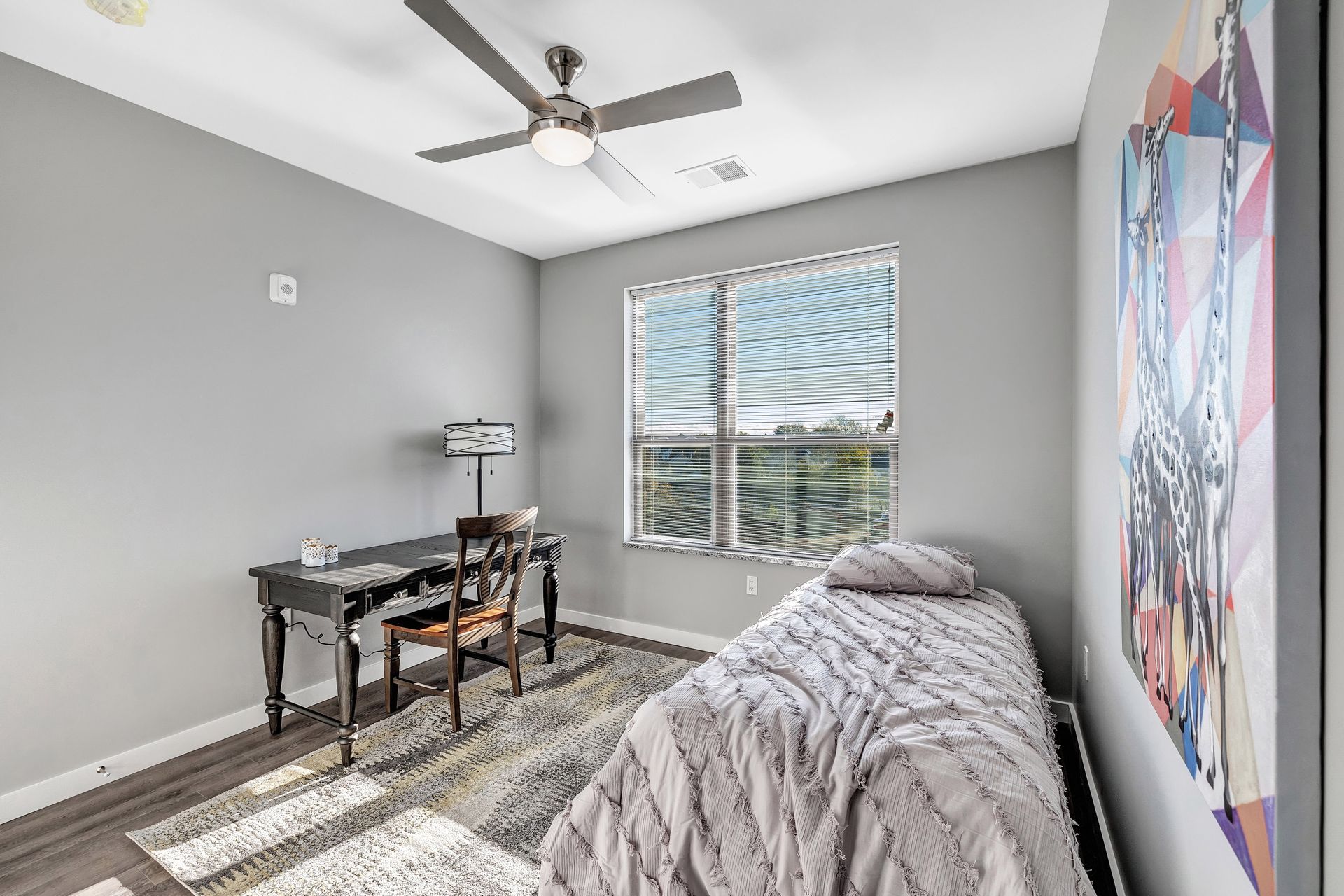 A bedroom with a bed , desk , chair and ceiling fan.