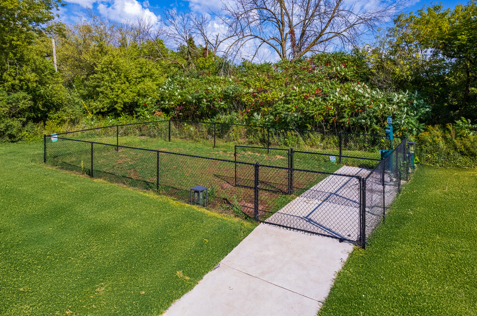 A concrete walkway leading to a dog park with a chain link fence.