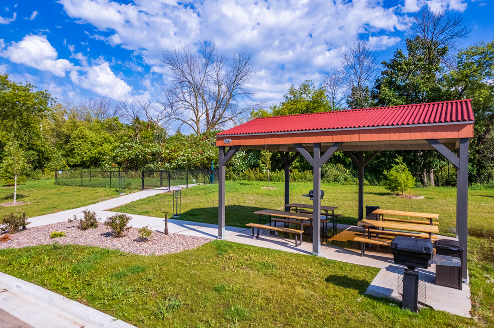 A picnic shelter with tables and benches and a grill in a park.