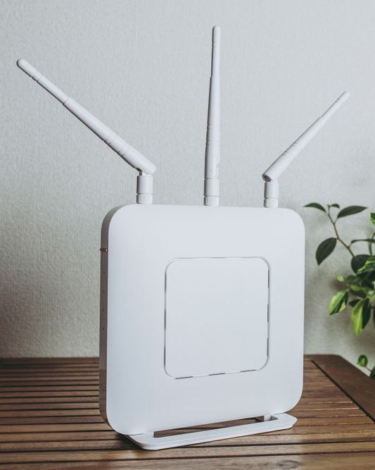 A White Router Is Sitting On A Wooden Table Next To A Plant — Dateline Computers Authorised Jaycar Reseller In Proserpine, QLD