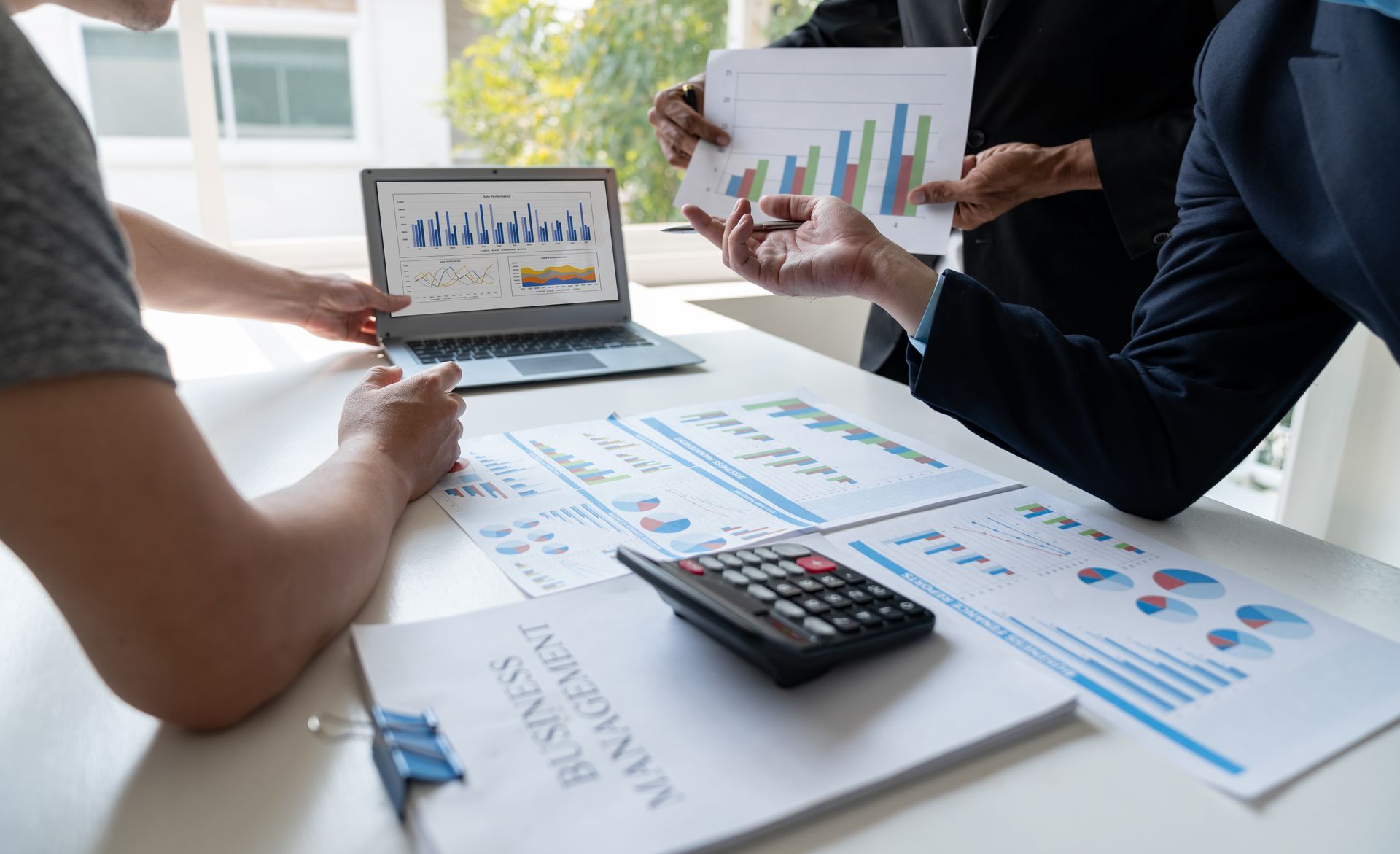 A group of people are sitting at a table looking at graphs and a laptop.