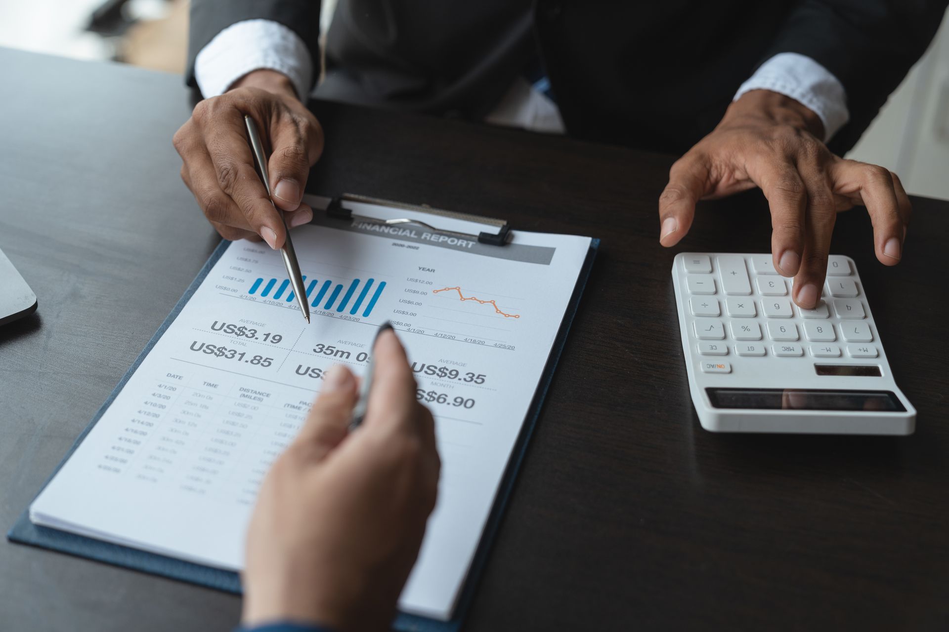 A man is using a calculator while a woman is pointing at a clipboard.