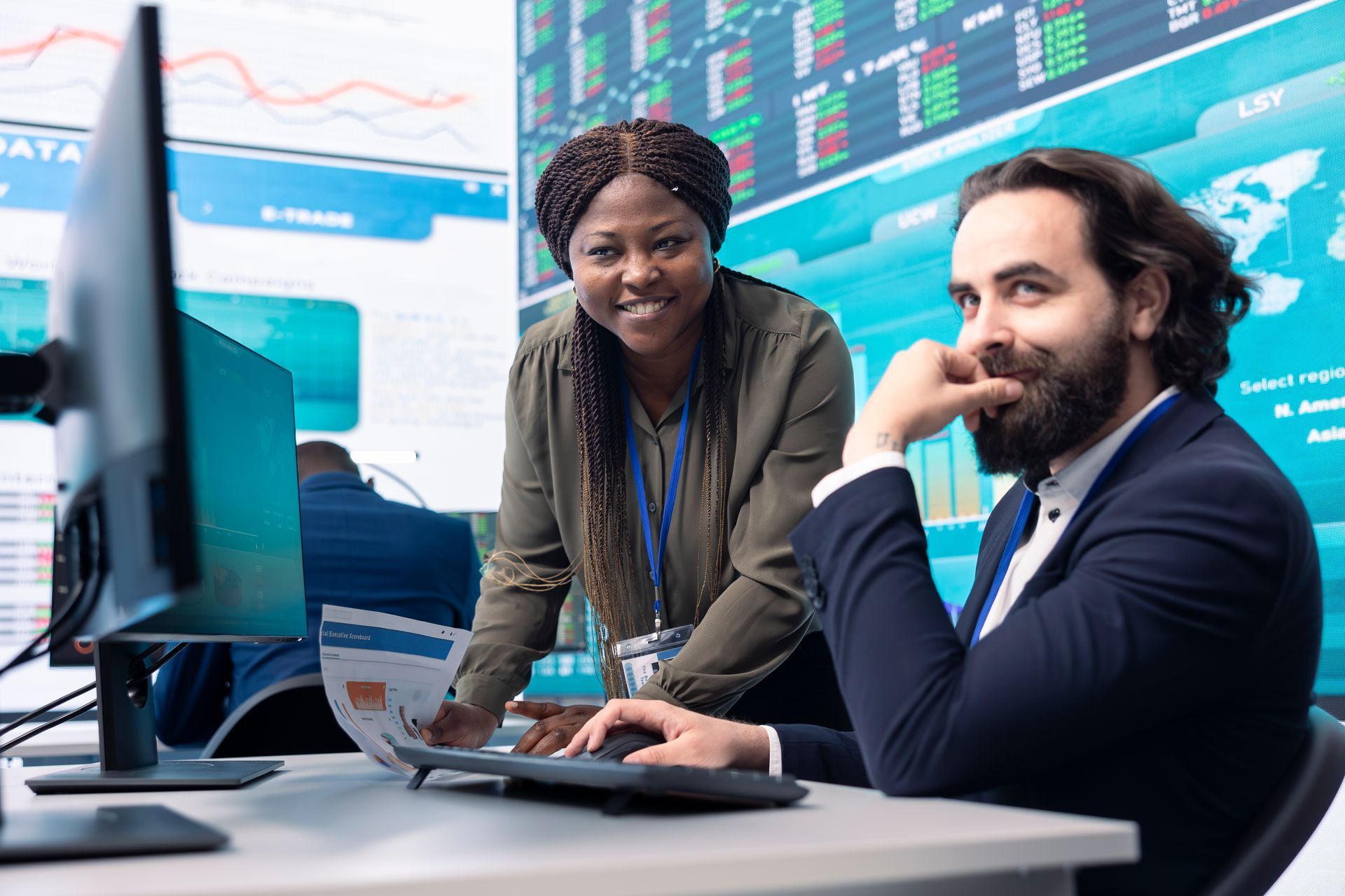 A man and a woman are sitting at a desk in front of a computer.