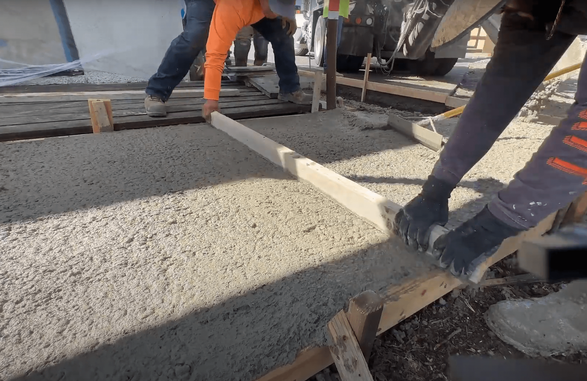 construction workers leveling concrete in a framed section of sidewalk for a concrete path