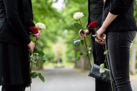 Due donne con rosa rossa e due uomini con rosa bianca fanno corridoio nel cimitero