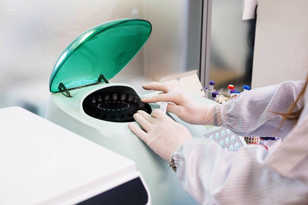 Una persona in camice e guanti utilizza una centrifuga in un laboratorio.