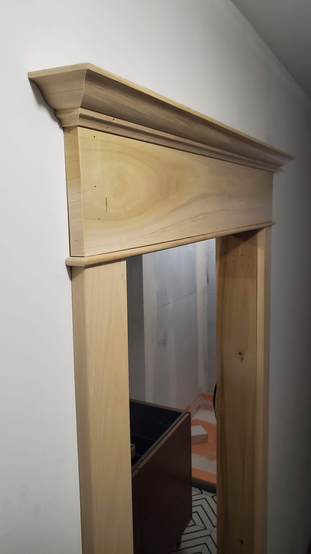 Wooden door frame, unfinished, installed in a white wall; view into a room with dark objects.