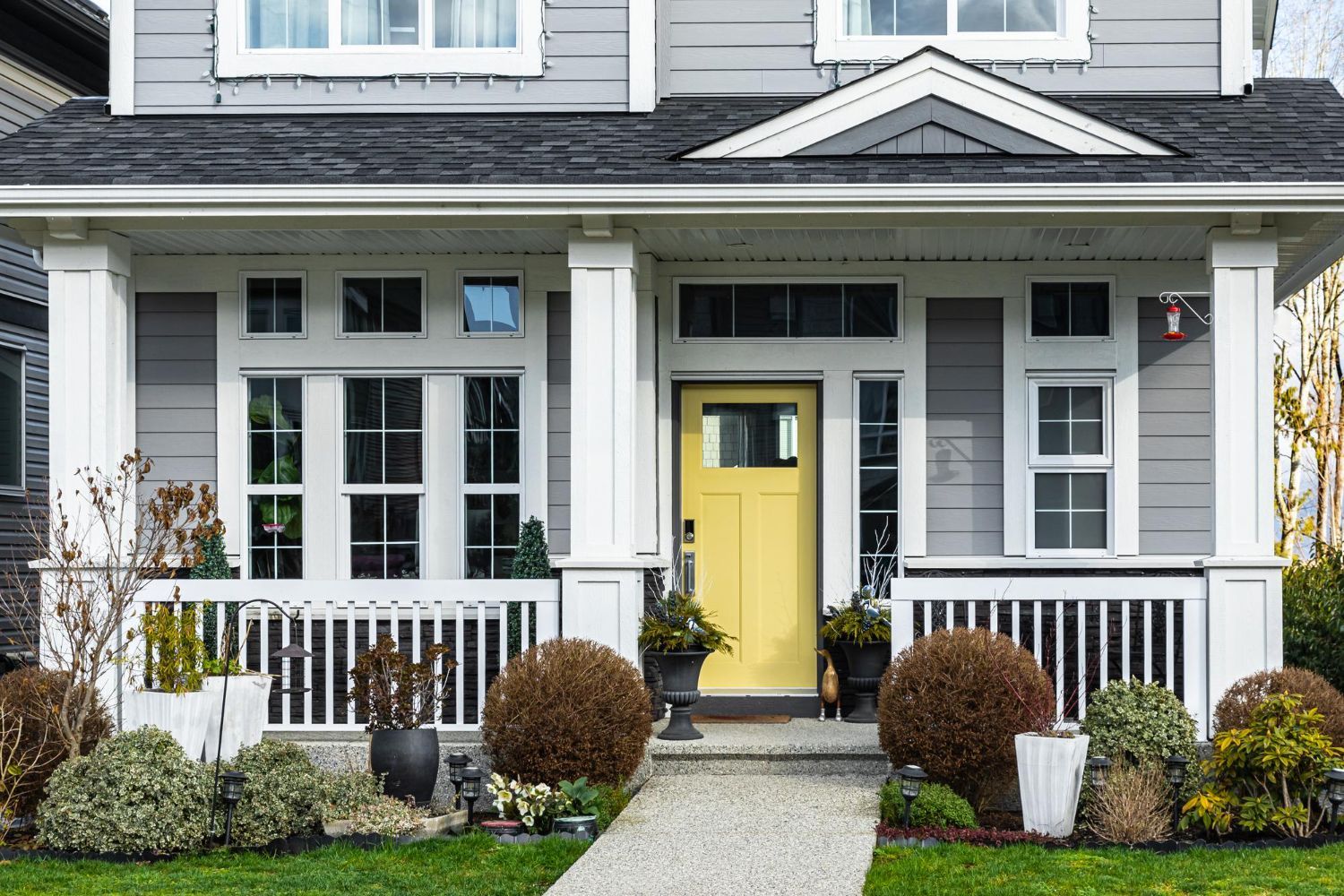 Gray house with white porch, yellow door, and manicured landscaping.