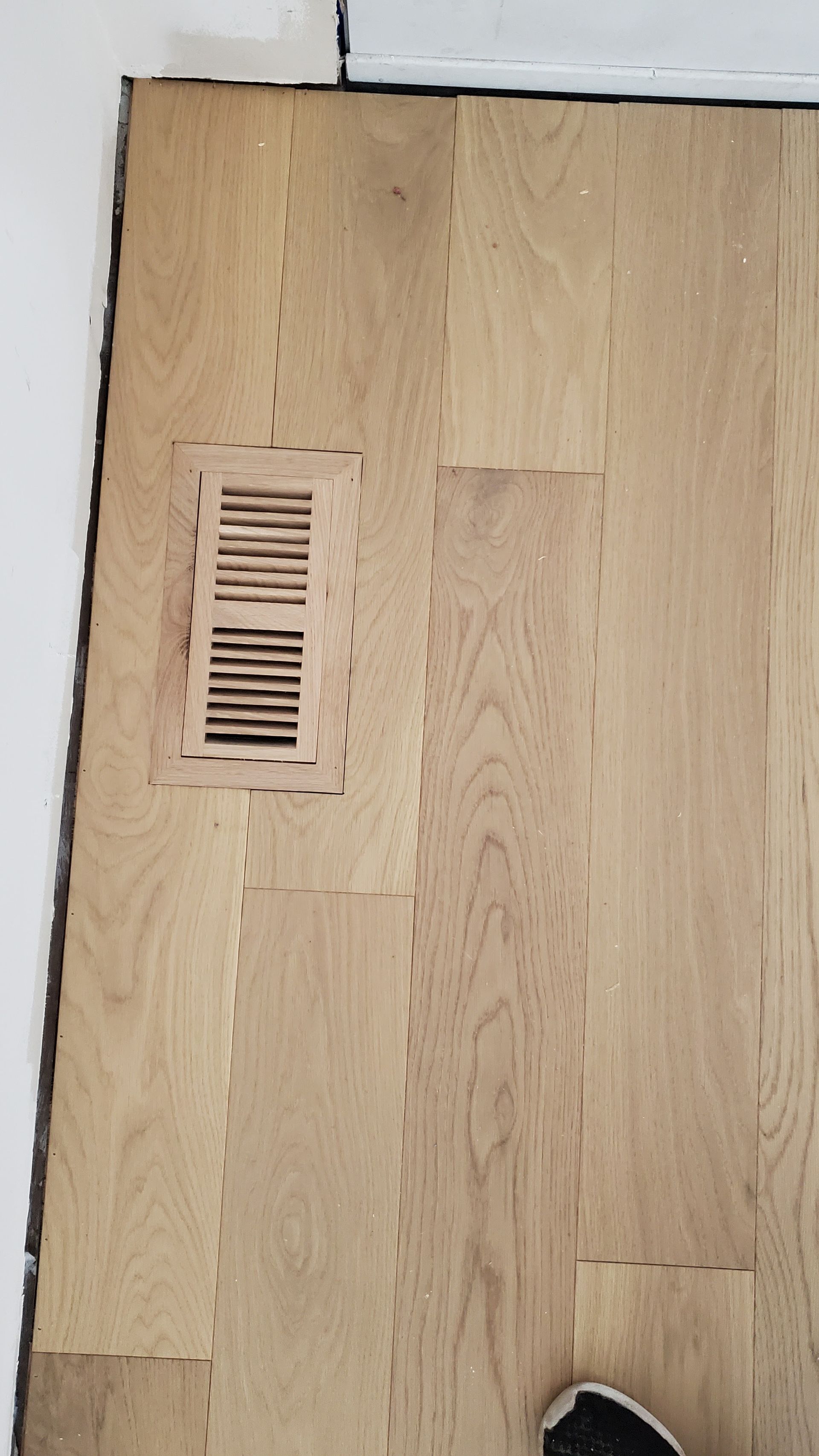 A person is standing on a wooden floor with a vent on it.