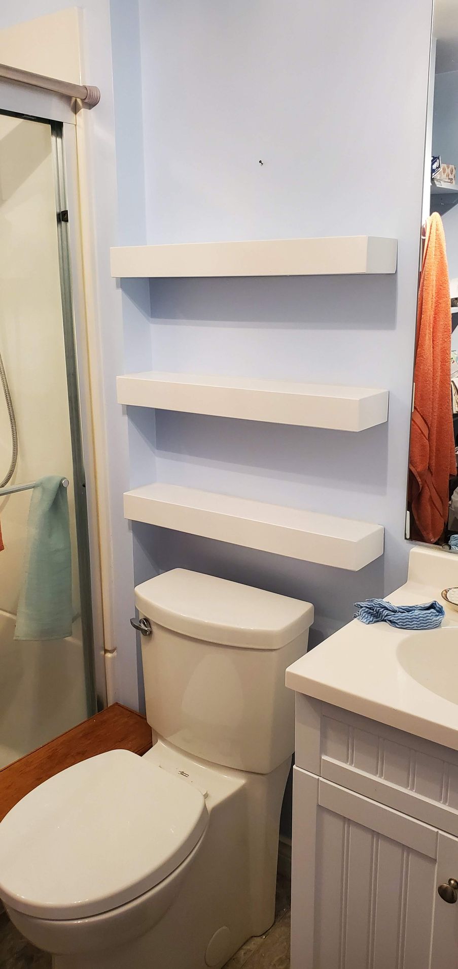 A bathroom with a toilet , sink , and shelves.