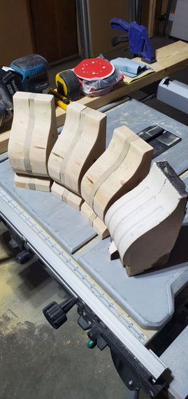Several light-colored wooden corbel blanks arranged in a fan shape on a workshop table.
