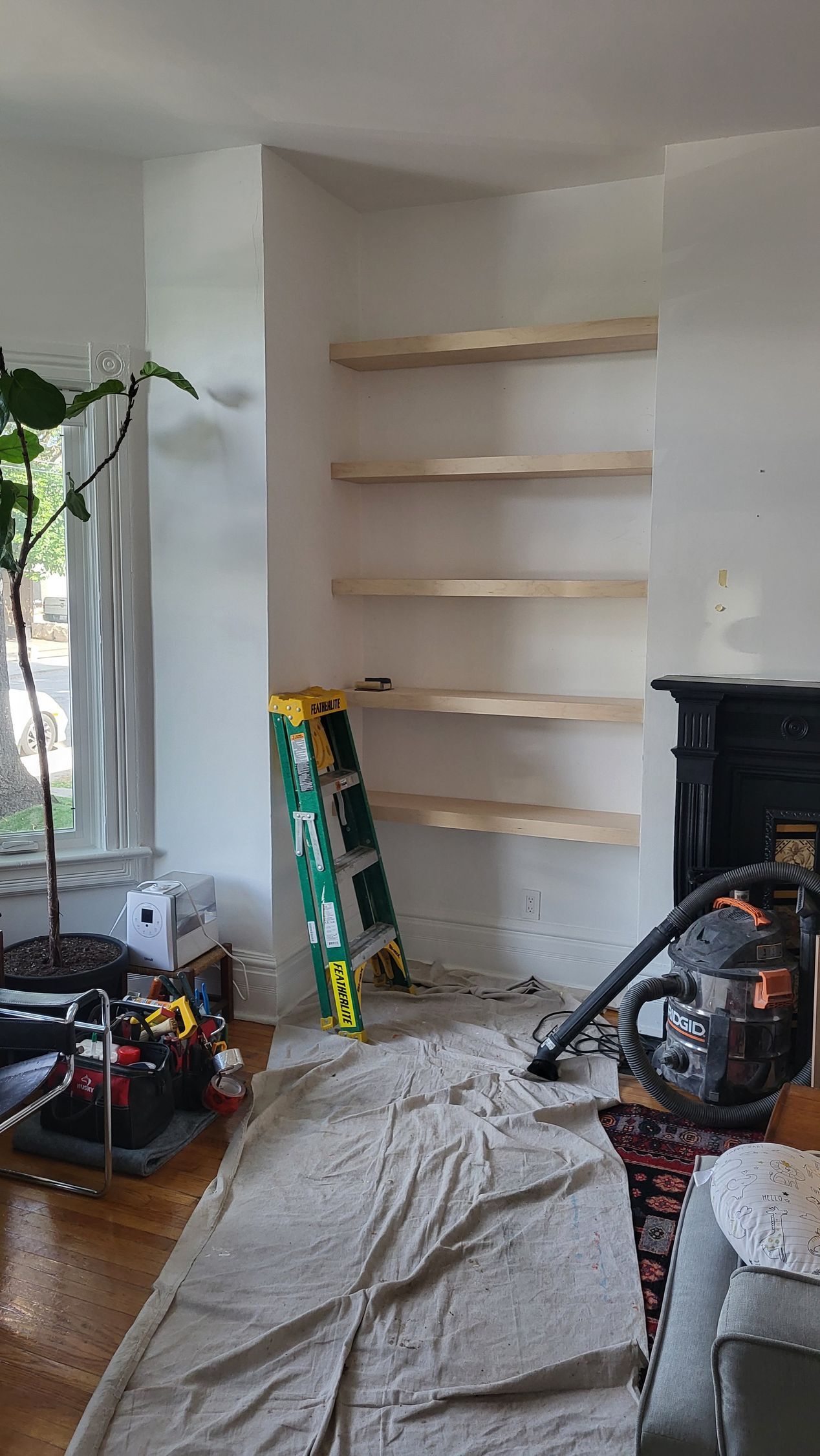 Interior with built-in shelves under construction; a ladder, tools, and a vacuum cleaner are in the area.