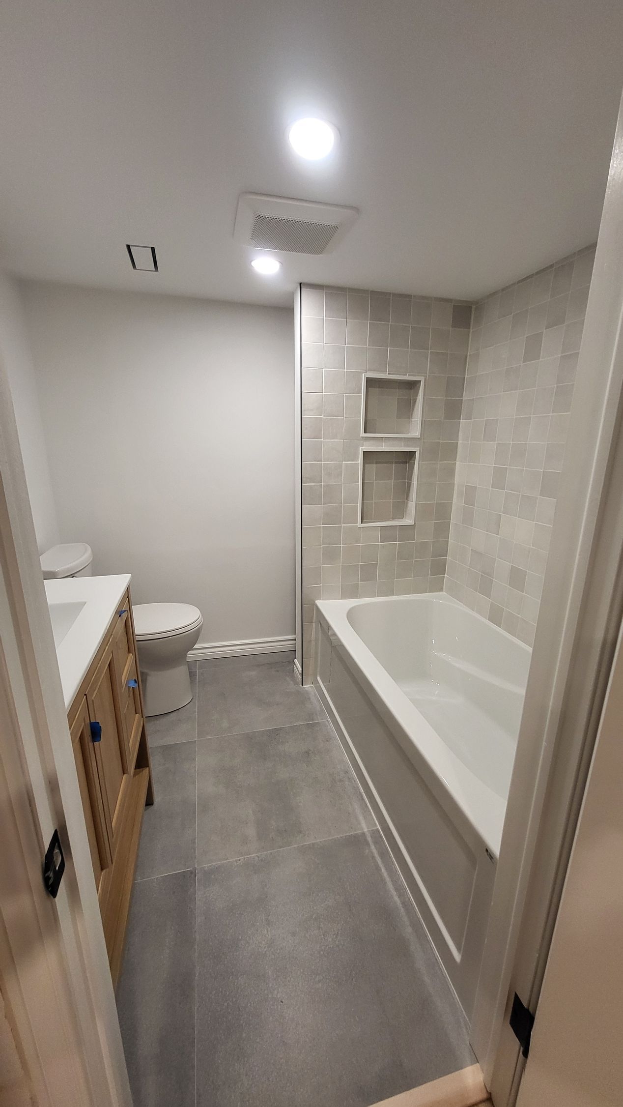 Bathroom with gray tile floor and walls, a bathtub, and a wooden vanity.