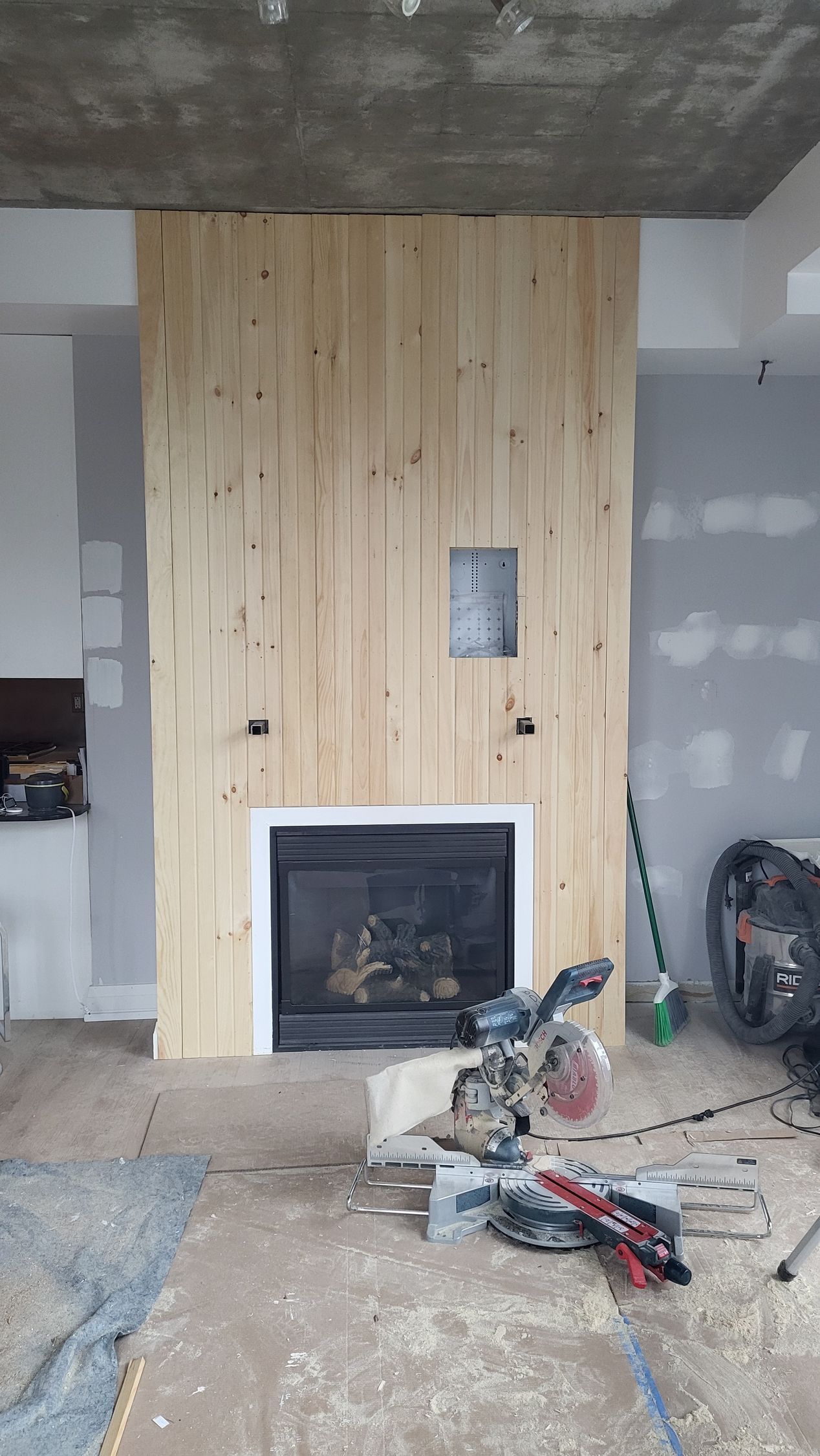 Fireplace with unfinished wooden paneling, a saw, and construction materials.