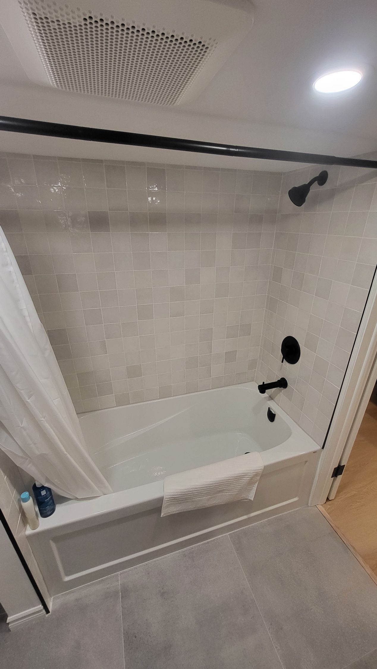 A modern bathroom with a white tub, black shower fixtures, and gray tiled walls.