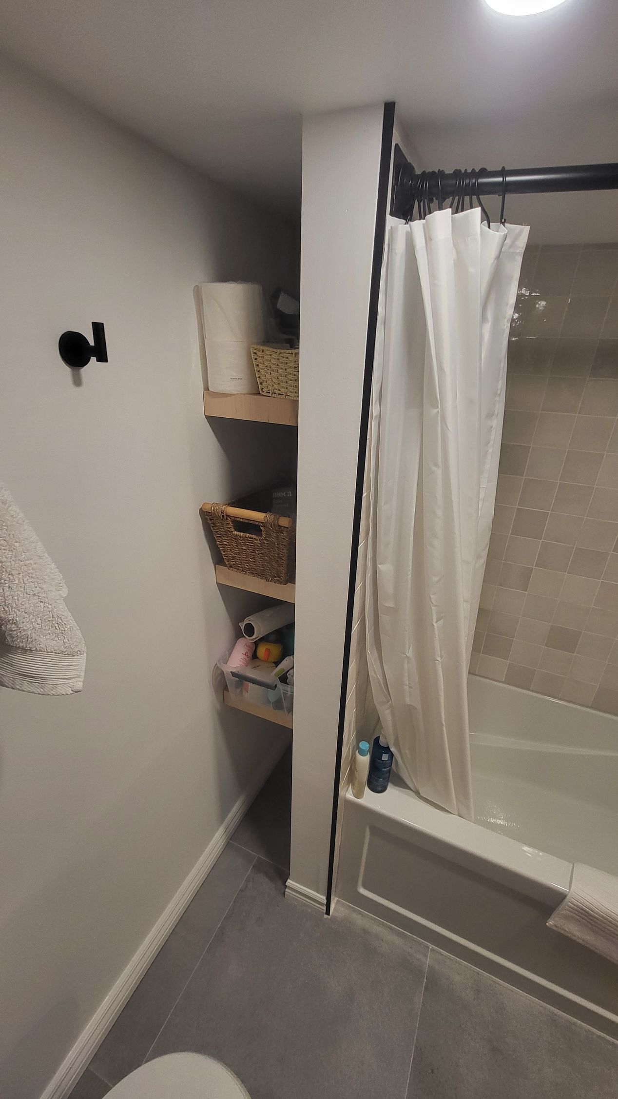 Bathroom with gray walls, small shelves, shower with curtain, and towel on the edge of the tub.