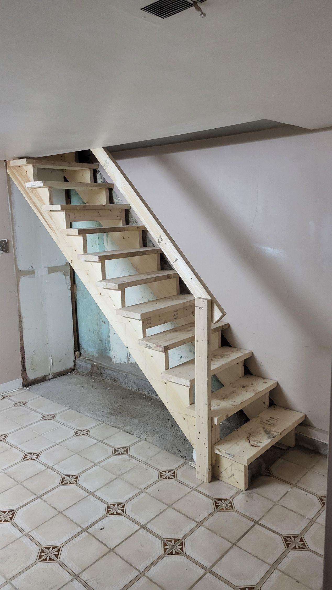 Wooden staircase in a room with tiled floor, leading up. The walls are plain, and the steps are unfinished.